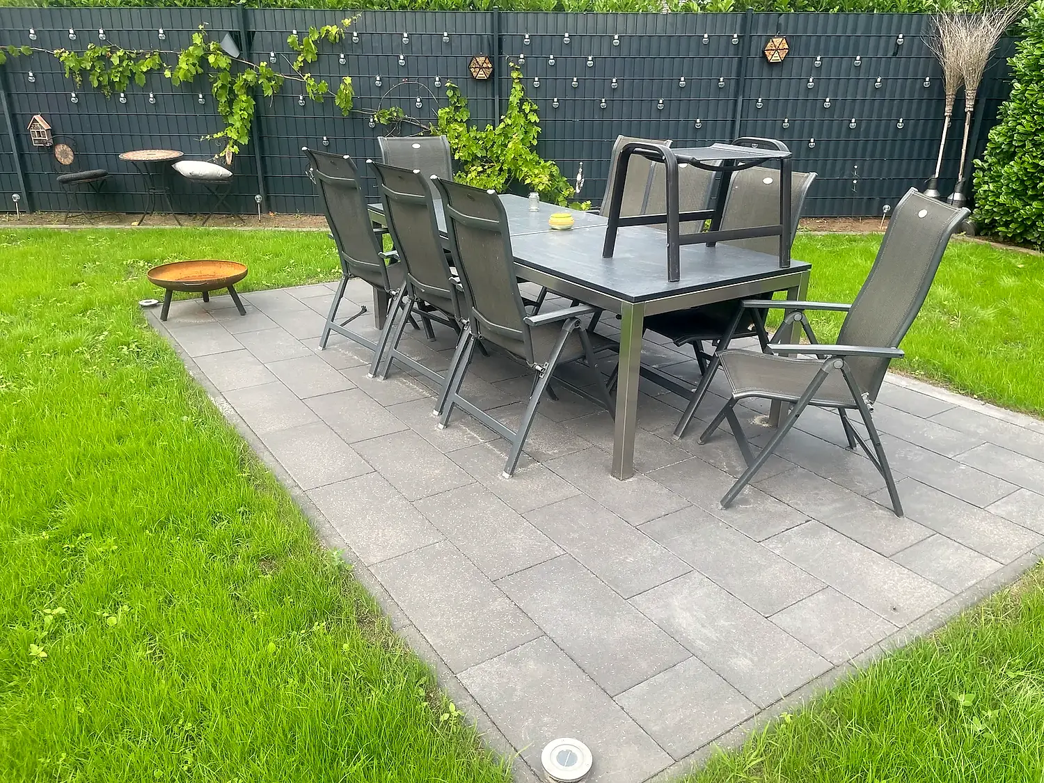 Betonpflaster-Terrasse mit Sitzgarnitur und angrenzender Rasenfläche
