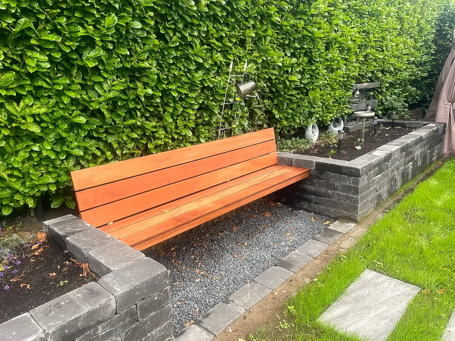 Gemauerter Sitzplatz mit Holzbank vor gepflegter Buchenhecke und Natursteineinfassung