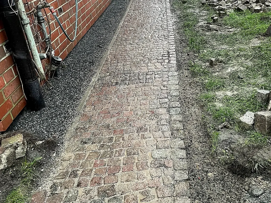 Fertig verlegter Natursteinweg aus Kopfsteinpflaster entlang der Hausfassade