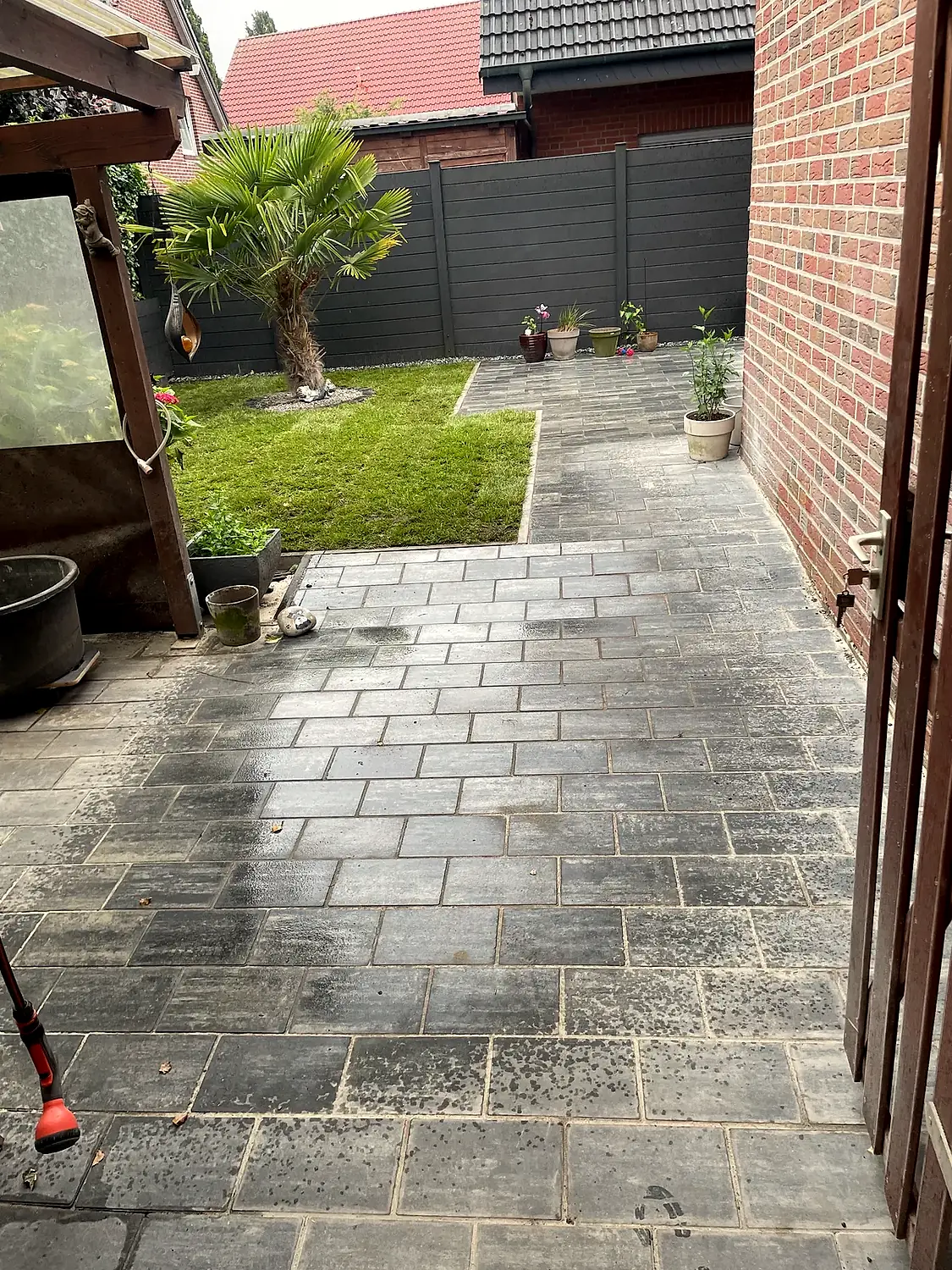 Gepflasterter Weg und Terrasse mit Palme entlang der Grundstücksgrenze